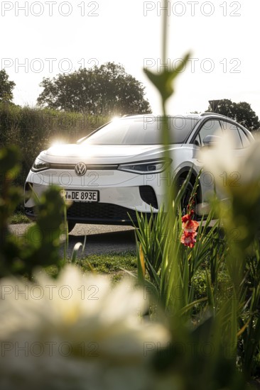 White car behind shade of blossoms, natural scene in sunlight, VW ID4 electric car, deer car sharing, Calw, Germany