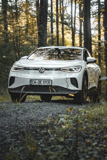 A white car is parked on a gravel path in the forest at dusk, VW ID4 electric car, Deer Carsharing, Calw, Germany