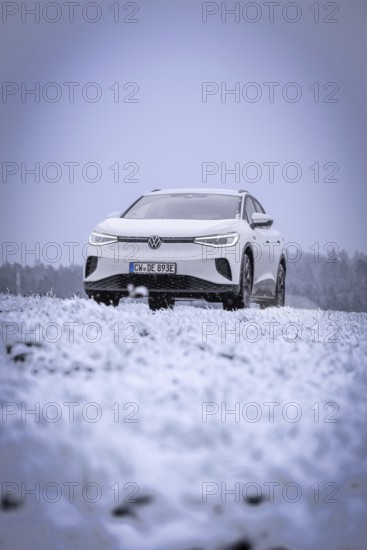 A white car is parked in a snowy field in dull winter weather, VW ID4 electric car, Deer Carsharing, Calw, Germany