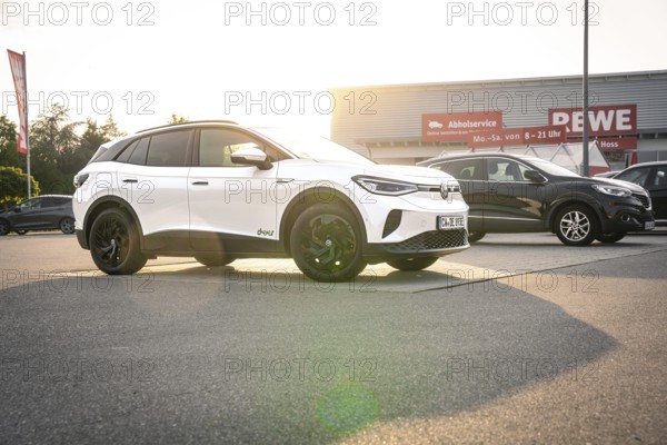 White vehicles in a parking lot in front of a shopping center at sunset, VW ID4 electric car, Deer Carsharing, Calw, Germany