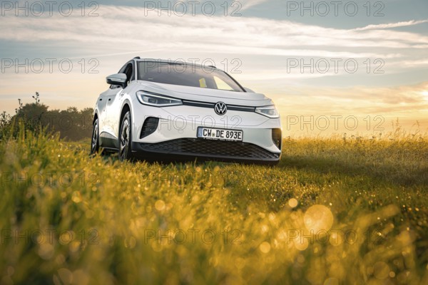 A white car is parked on a dewy meadow at sunrise, VW ID4 electric car, Deer Carsharing, Calw, Germany