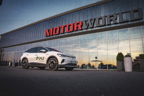 A car stands in front of a large building with glass façade during one evening, VW ID4 electric car, Deer Carsharing, Calw, Germany