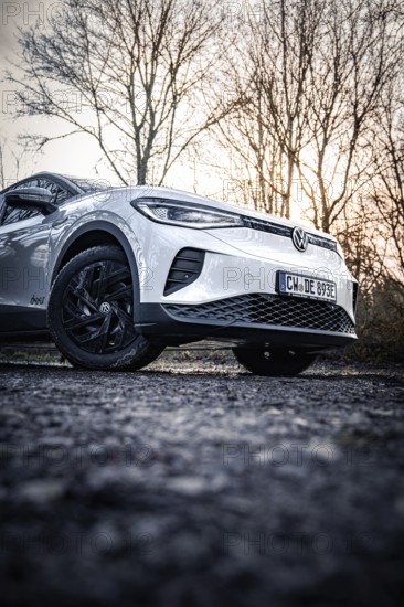 White car in front of bare trees at sunset in cold shades, VW ID4 electric car, Deer Carsharing, Calw, Germany