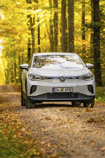 White car on a path through the golden autumn forest in sunlight, VW ID4 electric car, Deer Carsharing, Calw, Germany