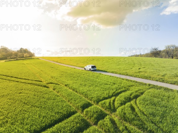 A car drives on a road through a green landscape under a cloudy sky, VW ID4 electric car, Deer Carsharing, Calw, Germany