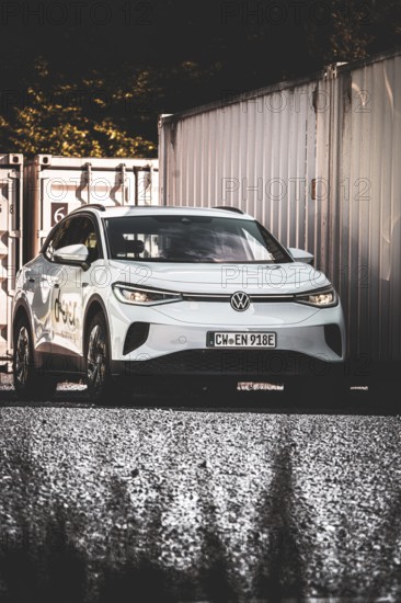 A car on a gravel field next to stacked containers in the shade, VW ID4 electric car, Deer Carsharing, Calw, Germany