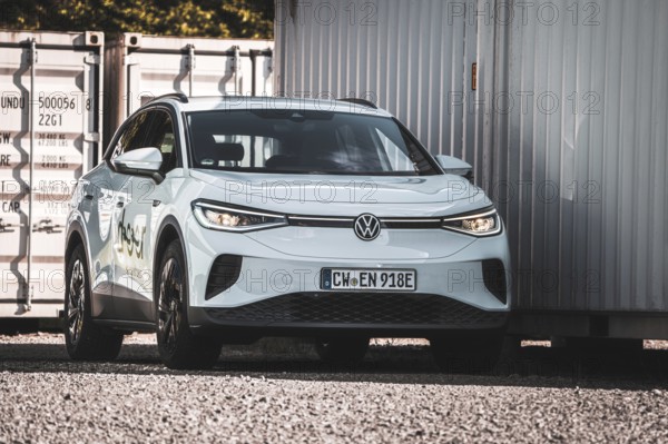 A white car is parked next to several containers on a gravel field, VW ID4 electric car, Deer Carsharing, Calw, Germany