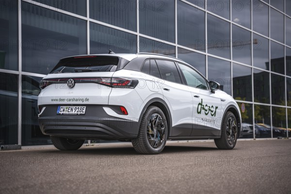 Rear of a white car in front of a modern glass façade in the city, VW ID4 electric car, Deer Carsharing, Calw, Germany