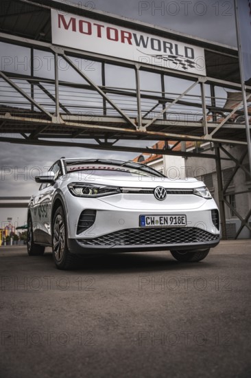 White car under scaffolding at Motorworld with cloudy sky, VW ID4 electric car, Deer Carsharing, Calw, Germany