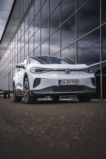 White car in front of a modern glass façade in an urban environment, VW ID4 electric car, Deer Carsharing, Calw, Germany