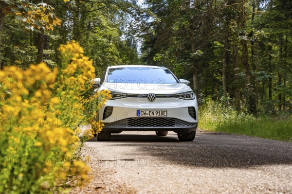 White Volkswagen on a road in the forest next to yellow flowers, VW ID4 electric car, Deer Carsharing, Calw, Germany