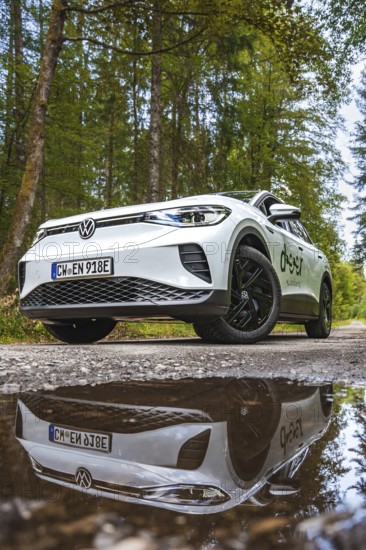 A white car is reflected in a puddle of water on a forest road, VW ID4 electric car, Deer Carsharing, Calw, Germany