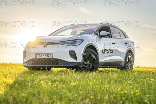 A white car is parked on a blooming meadow at sunset, VW ID4 electric car, Deer Carsharing, Calw, Germany
