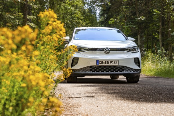 White Volkswagen on a forest road next to yellow flowers, VW ID4 electric car, Deer Carsharing, Calw, Germany