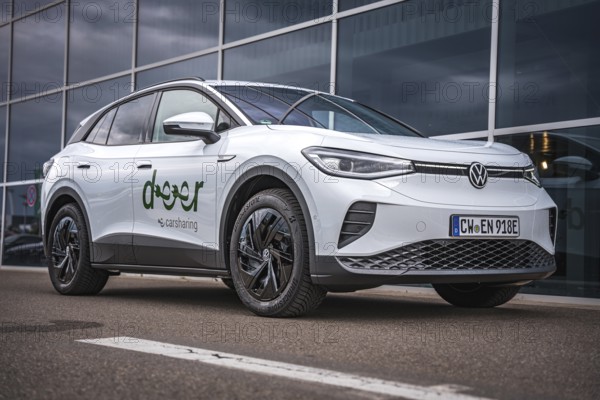 Side view of white car in front of glass façade with blue sky, VW ID4 electric car, Deer Carsharing, Calw, Germany