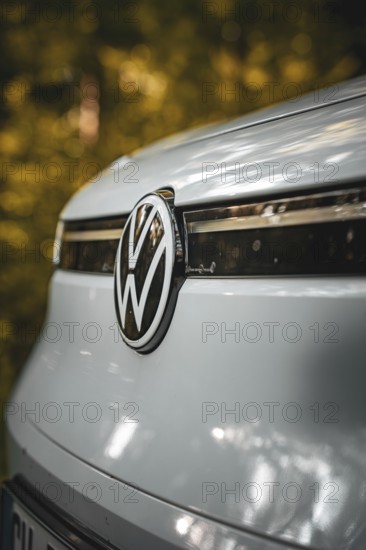 Close-up of VW logo on the front of a white car with forest in the background, VW ID4 electric car, deer car sharing, Calw, Germany