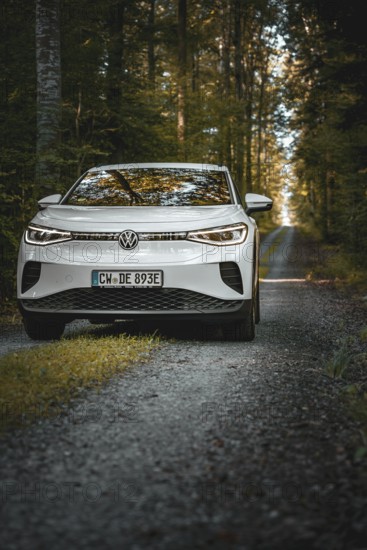 White car on a forest path surrounded by tall trees in morning light, VW ID4 electric car, deer car sharing, Calw, Germany