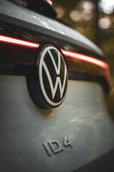 VW logo with rear light of a car in warm light in the forest, VW ID4 electric car, Deer Carsharing, Calw, Germany