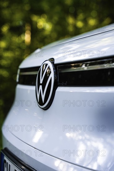 Close-up of VW logo on the front of a white car in the forest in daylight, VW ID4 electric car, Deer Carsharing, Calw, Germany