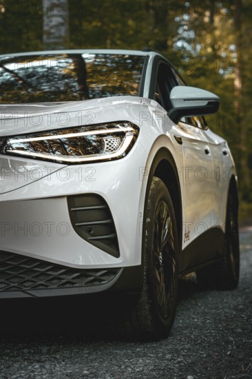 Close-up of white car in forest with emphasis on headlights, VW ID4 electric car, deer car sharing, Calw, Germany