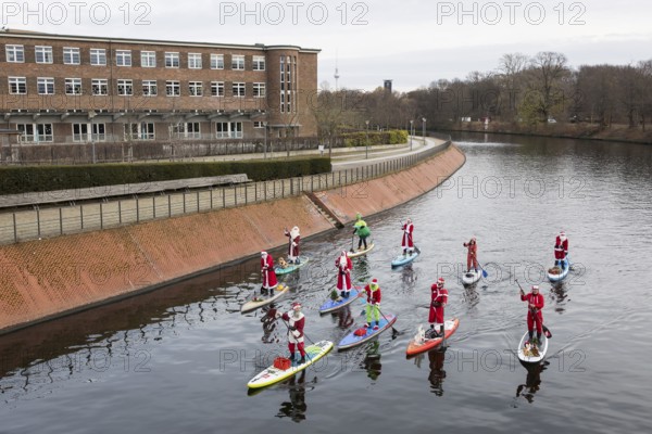 Water sports enthusiasts dressed up as Santa Claus ride SUPs on the Spree am Park at the presidential triangle in Berlin on 30.11.2025
