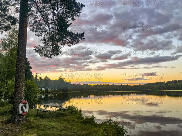 A calm lake at sunset with cloud reflection and trees and red white lifebuoy in the foreground, Hällefors, Örebro, Sweden
