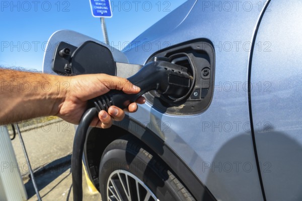 Hand inserting power cable into electric vehicle at a vehicle charging station, promoting sustainable transportation and eco friendly practices