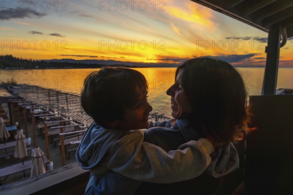 Mother and son embracing warmly while enjoying a breathtaking sunset over the serene waters of qualicum beach on vancouver island during summer vacation