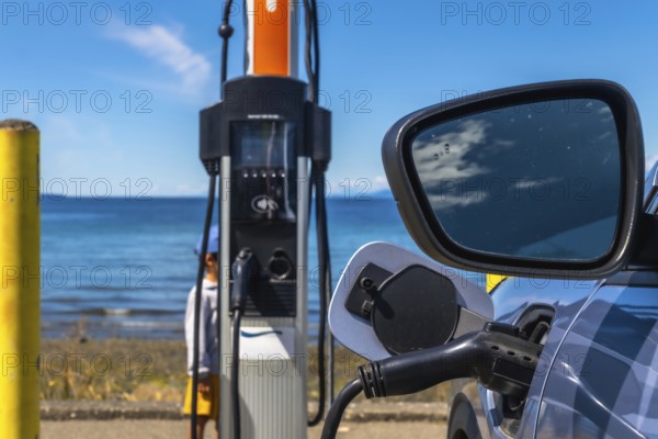 Modern electric vehicle connected to a charging station on the coast with a beautiful ocean view, promoting sustainable transportation and clean energy