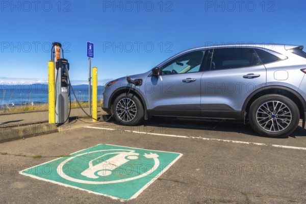 Silver electric car charging at a station by the sea, showcasing a picturesque ocean view while promoting sustainable transportation and clean energy solutions for the future