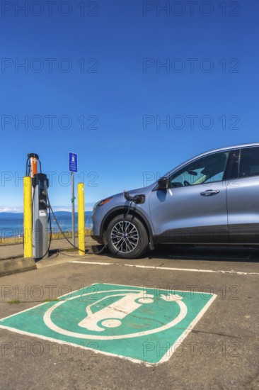 Modern electric car charging at a seaside station on a bright sunny day, highlighting the importance of sustainable transportation and the benefits of clean energy solutions