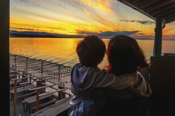 Mother and child share a tender moment, gazing at a vibrant sunset over the tranquil waters of qualicum beach on vancouver island, canada, capturing the essence of summer serenity