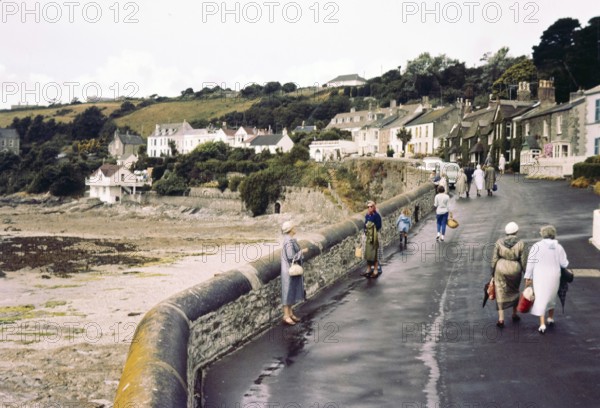 People walking on coastal promenade road, Lower Castle Road, St Mawes, Cornwall, England, UK, c 1960