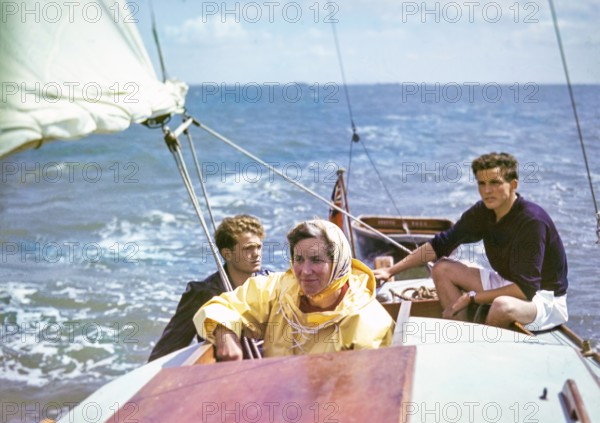 Woman sailing on small yacht with two young men, UK 1950s