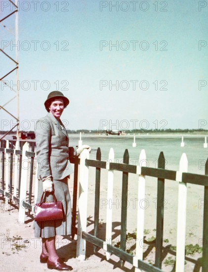 Portrait of smartly dressed woman wearing a suit and hat standing at an airport c 1956