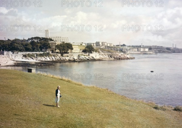 Woman walking on grass by the coast Plymouth, Devon, England, UK c 1962