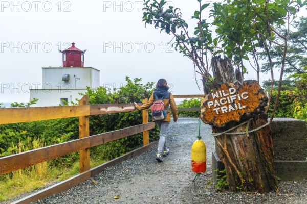 Female tourist walking along the gravel path of the wild pacific trail near amphitrite point lighthouse in ucluelet, british columbia, surrounded by lush greenery