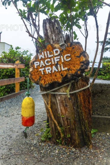 Rusty sign marking the wild pacific trail in ucluelet, british columbia, featuring a weathered wooden post, nautical rope, and a hanging buoy