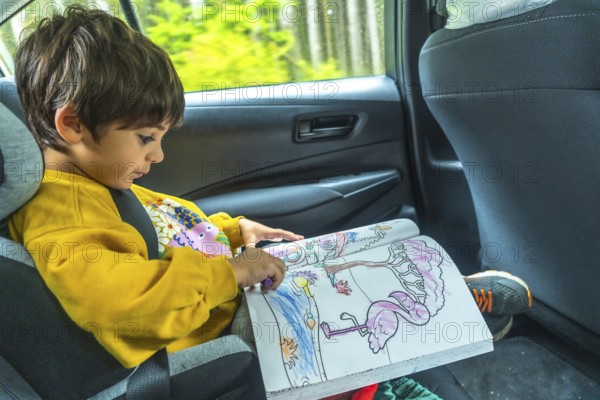 Young child concentrating on a coloring book in a car seat during a scenic drive through the rainforest on vancouver island, capturing a peaceful moment of creativity