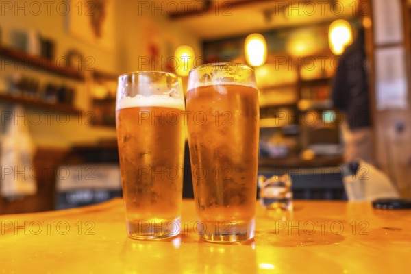 Two glasses of cold craft beer sit on a wooden table in a cozy pub in ucluelet, british columbia, with a blurred background hinting at the lively atmosphere