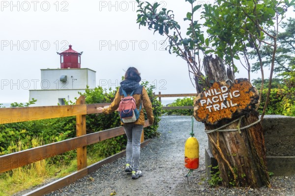 Female tourist walking towards amphitrite point lighthouse on the wild pacific trail near ucluelet on vancouver island, british columbia, canada, on a cloudy day