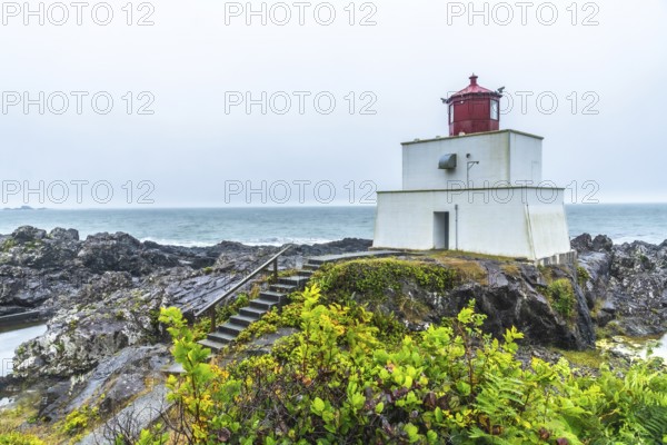 The amphitrite point lighthouse stands on the rocky coast of ucluelet, vancouver island, providing a beacon of safety for ships navigating the pacific ocean on a cloudy day