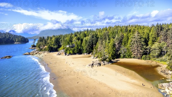 Aerial view of mackenzie beach in tofino, vancouver island, british columbia, canada, showing tourists enjoying the sandy beach, blue ocean, and lush green forest on a sunny summer day