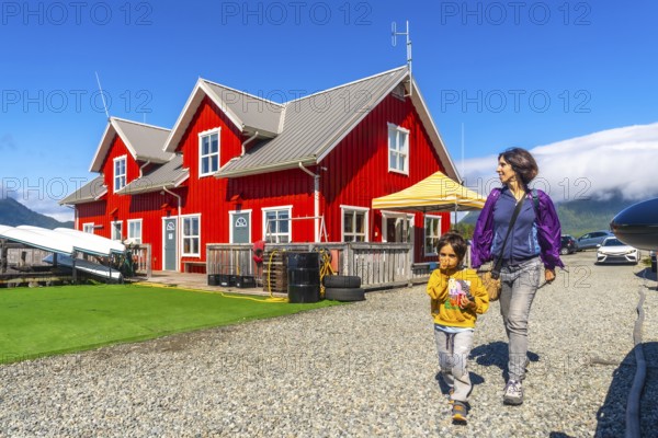 Tourists walking near a vibrant red building in tofino, a charming district on vancouver island's west coast, enjoying a sunny summer vacation