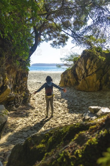 Female tourist with open arms enjoying breathtaking view of mackenzie beach after hiking through lush rainforest trail in tofino, vancouver island, british columbia, canada