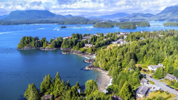Aerial view capturing tofino on vancouver island, showcasing lush green forests, blue ocean waters, boats, and mountains under a sunny summer sky