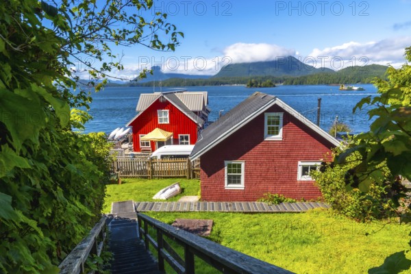 Wooden stairs leading down to red houses in tofino, british columbia, canada with clayoquot sound and green mountains in the background on a beautiful summer day