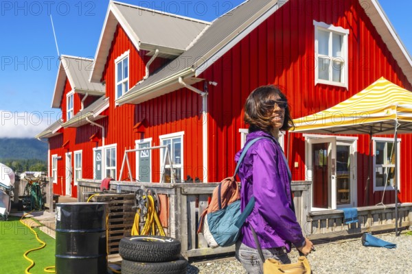 Female tourist walking near a red wooden building in tofino, a popular travel destination on vancouver island, british columbia, canada, enjoying summer vacation