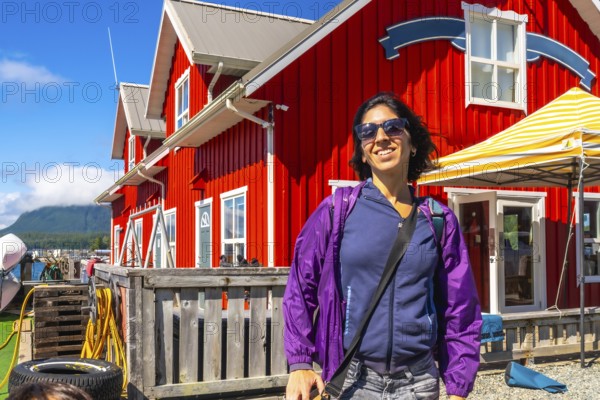 Happy tourist smiling in front of a characteristic red building in tofino, a popular travel destination on vancouver island, british columbia, canada, during a sunny summer day