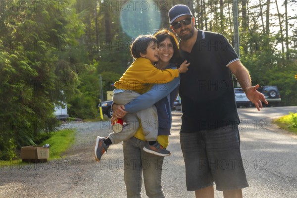 Happy family of tourists enjoying their summer vacation in tofino, vancouver island, british columbia, canada, with the mother carrying their son and the father gesturing to the side